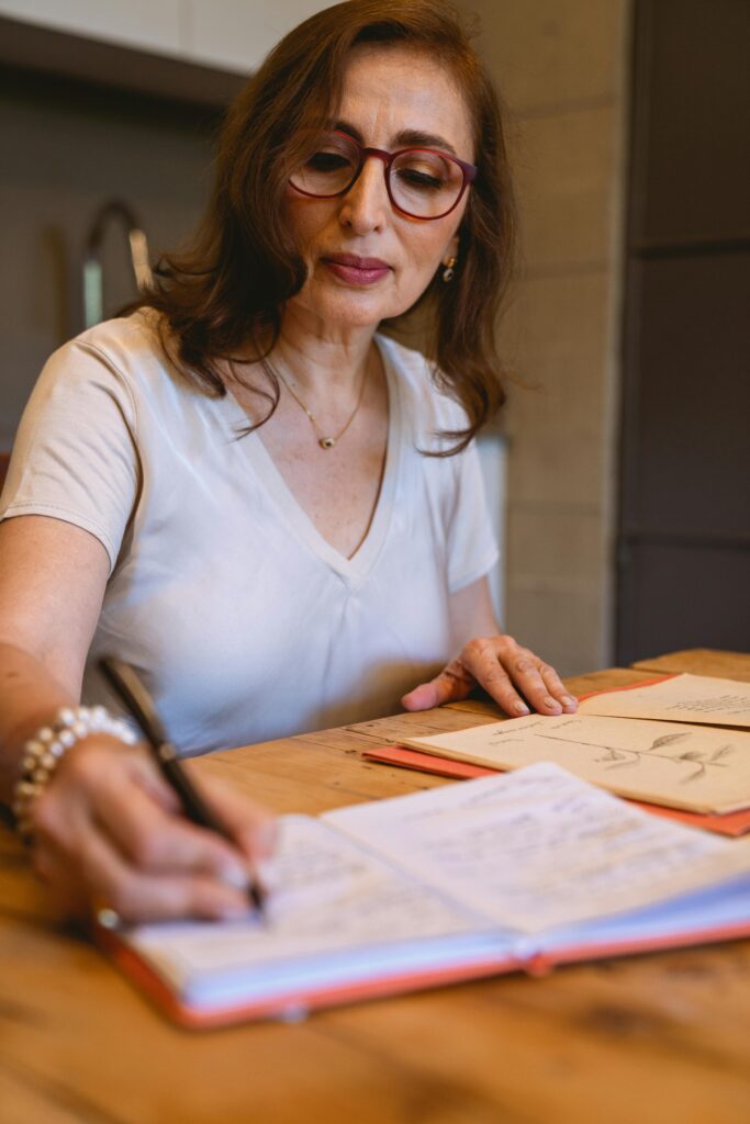 Woman in white shirt with eyeglasses writing on notebook